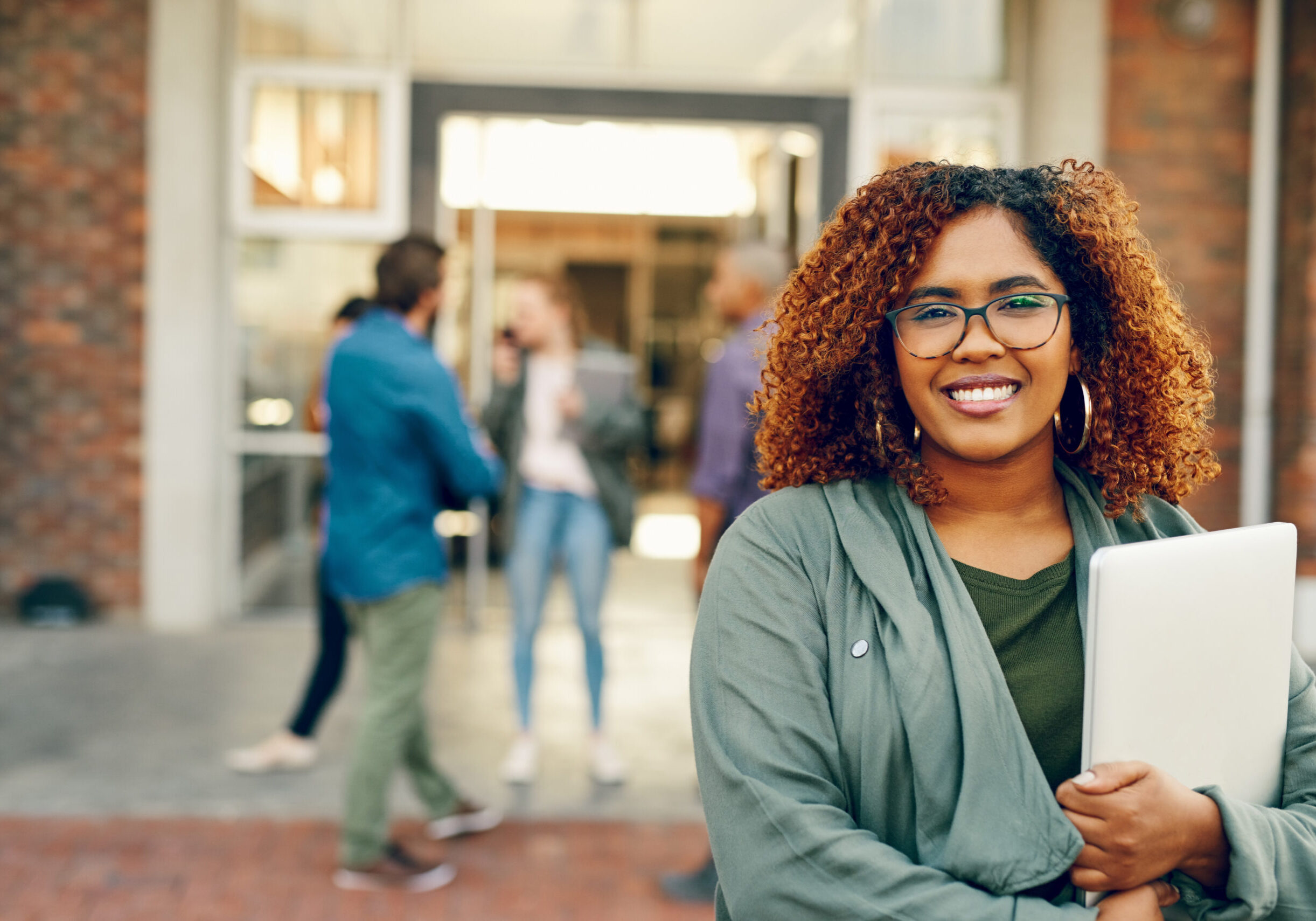 Portrait of a happy young woman holding a laptop outdoors on campus.